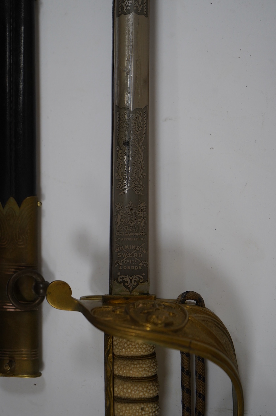 A George VI naval officer’s dress sword by Wilkinson (unnumbered), with regulation brass hilt with folding guard, engraved P.A.R. Gould R.N., bullion dress knot, in its brass mounted leather scabbard and contained in its